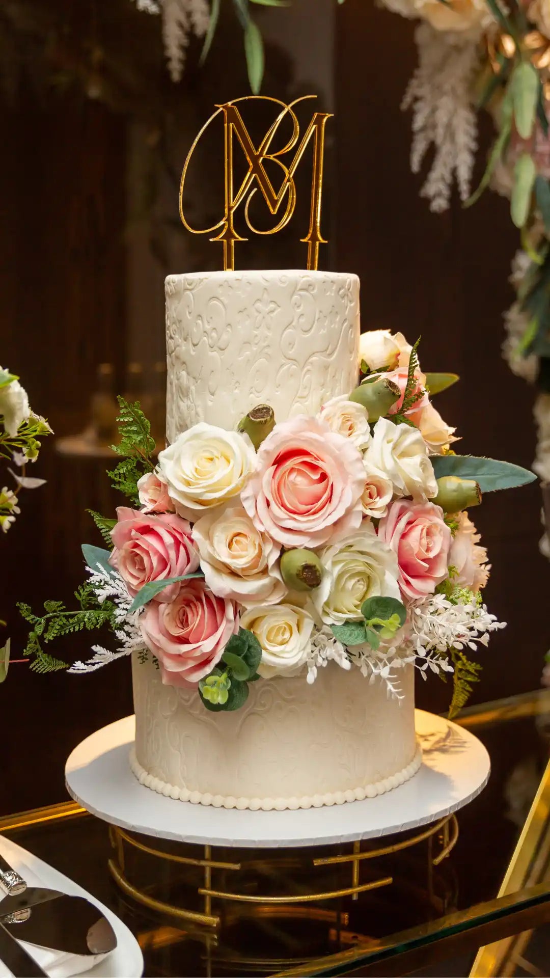 Three-tiered wedding cake with floral decorations and gold monogram topper.